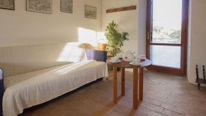 Une pièce chaleureuse avec un canapé blanc, une petite table ronde sur laquelle est disposé un service à thé, et des œuvres d’art encadrées accrochées au mur.