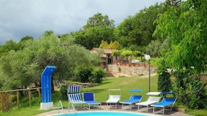 Une piscine dotée de chaises longues et d’un toboggan, entourée de verdure et avec un bâtiment en pierre en arrière-plan.