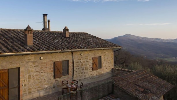 Un bâtiment en pierre avec un toit en tuiles, un balcon avec des chaises et une vue sur les montagnes.