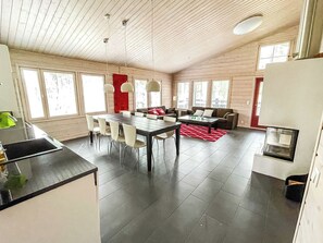 A modern kitchen with a dining area, large windows, and a red rug.