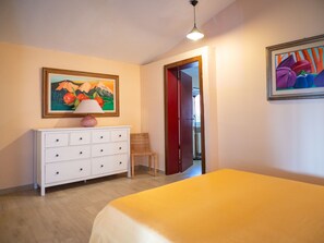 Une chambre à coucher avec un lit, une commode, une lampe, une chaise et deux tableaux accrochés aux murs.