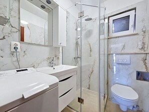 Un baño moderno con cabina de ducha de vidrio, un lavabo blanco, un espejo y un inodoro.