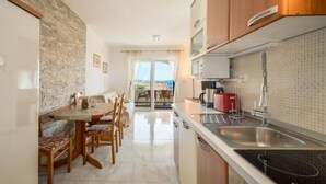 A modern kitchen with a built-in microwave, a sink, and a stove. There is a dining area with a table and chairs, and a view of the sea through the glass doors.