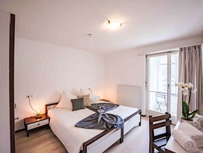 A bedroom with a bed, bedside tables, a chair, a window with curtains, and a view of the outside. - Chesa Ova Cotschna 606 by Interhome (St. Moritz)