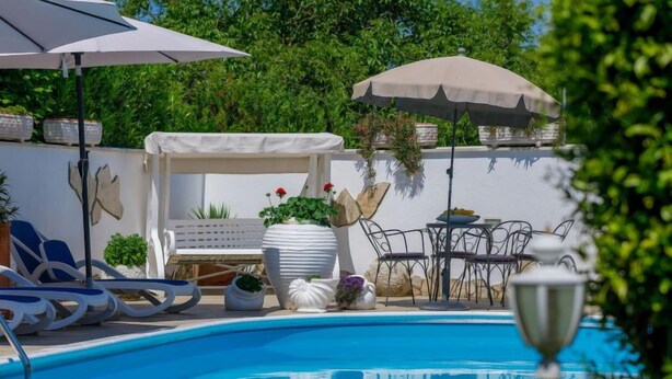 Une piscine entourée de chaises longues et de parasols, agrémentée de plantes en pot et d’une pergola.