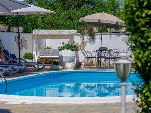Una piscina con sillas de descanso y sombrillas, rodeada de plantas en macetas y una pérgola.