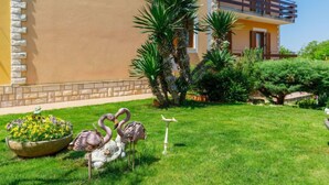 Un bâtiment à la façade jaune, doté d’un balcon et agrémenté d’un jardin bien entretenu où l’on peut admirer des flamants roses et une sculpture d’oiseau.