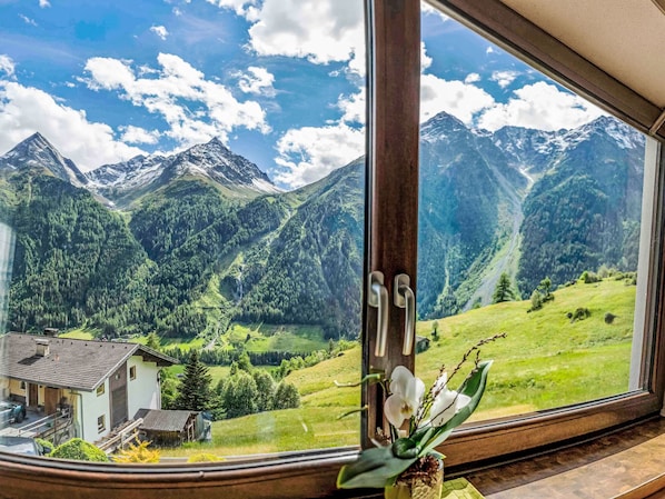 A window with a view of a mountain landscape, a wooden door, and a vase with flowers.