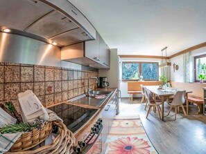 A modern kitchen with a built-in stove, a dining area with a wooden table and chairs, and a view of the outdoors through a large window.