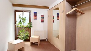 Een kamer met een bureau, een plant, een radiator, een spiegel en een kledingkast.