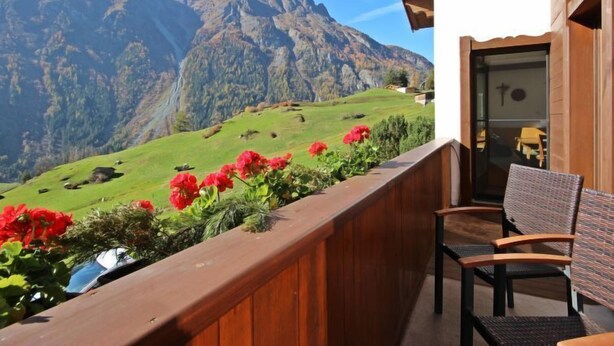 Een balkon met houten hekwerk, een stoel en uitzicht op een bergketen.