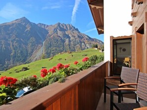A balcony with a wooden railing, a chair, and a view of a mountain range.