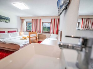 A hotel room with a bed, a chair, a desk, and a window with curtains.