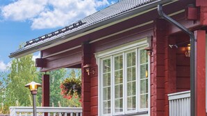 Een rode houten woning met een witte veranda, een bloemenmand en een witte balustrade.