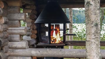 A wood-burning stove in a log cabin with a view of a lake.