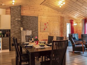 Un coin repas avec une table en bois dressée pour quatre personnes, entourée de chaises, avec un mur en pierre et un plafond en bois.
