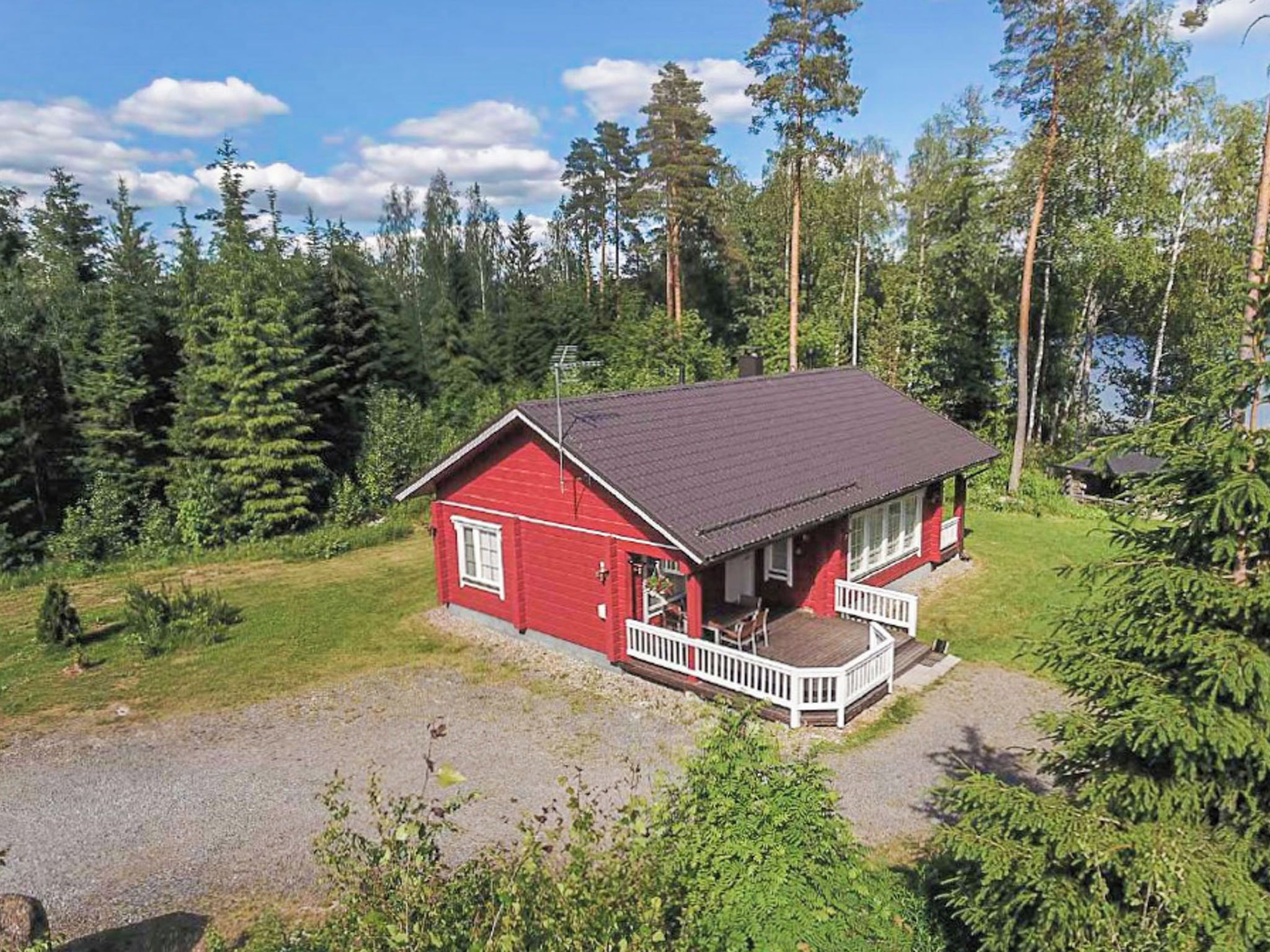 Punainen mökki, jossa on kuisti, ja sen ympärillä tiheä metsä sekä kirkas taivas.