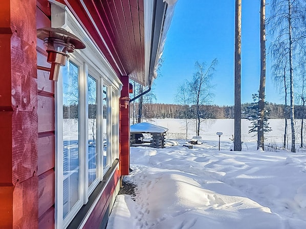 Une cabane en bois dotée de grandes fenêtres, une cour enneigée et un ciel bleu dégagé.