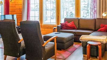 Interior acogedor de una cabaña de troncos con un sofá, sillones, una mesita y una ventana con vistas.