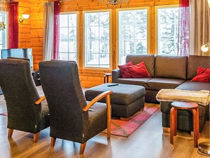 A cozy log cabin interior with a sofa, armchairs, a small table, and a window with a view.