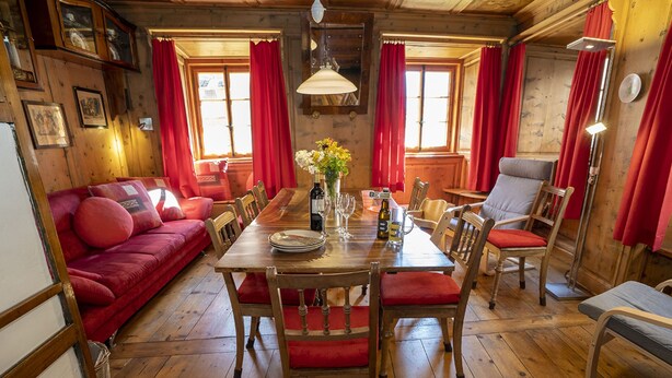 Ein gemütliches Holzinterieur mit einem für vier Personen gedecktem Esstisch, umgeben von roten, gepolsterten Stühlen.