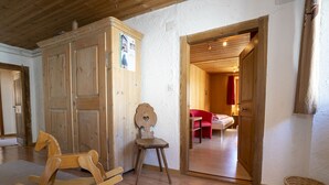 Ein hölzernes Schaukelpferd, ein kleiner Holzstuhl und eine Tür zu einem Schlafzimmer mit einem Bett und einem roten Sessel.