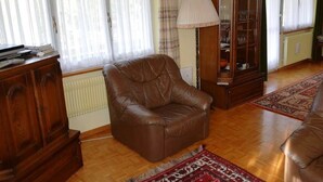 Una sala de estar con un sillón de cuero marrón, un aparador de madera y una vitrina de vidrio.