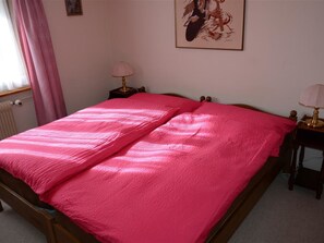 Ein Schlafzimmer mit einem hölzernen Bett, pinkener Bettwäsche, einem Nachttisch mit Lampe und einem gerahmten Bild an der Wand.