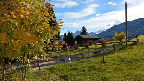 Paisaje rural con una valla de madera, una casa y montañas al fondo.