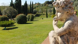 Una estatua de una figura sentada en un jardín con césped cuidado, árboles y arbustos.