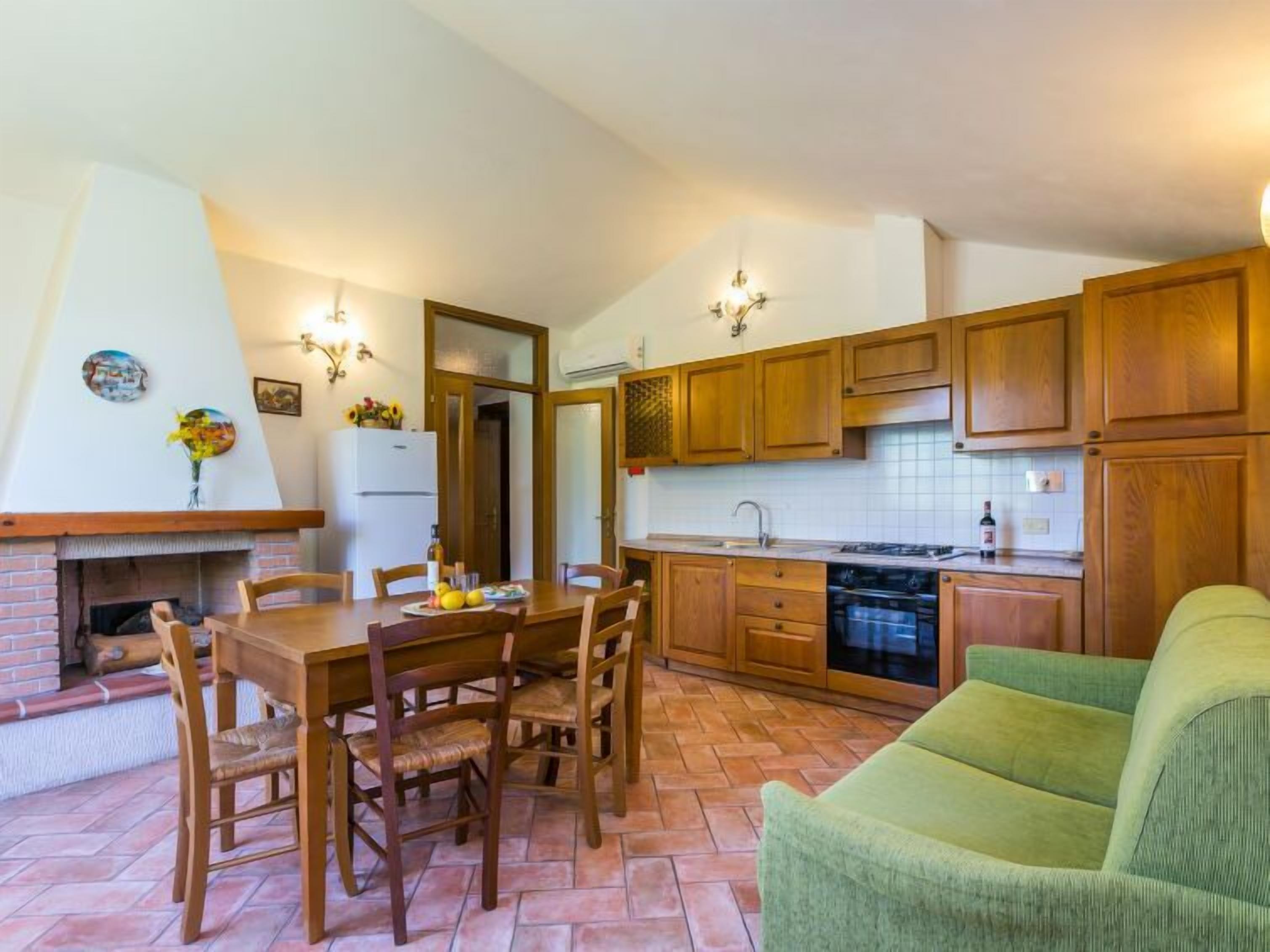 Una cucina compatta con mobili in legno, un tavolo da pranzo con sedie, forno integrato e un divano verde.