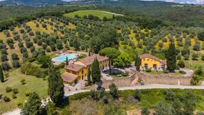 Una villa rodeada de olivares y una piscina, con un muro de piedra y vistas a colinas distantes.
