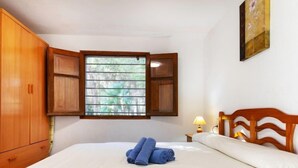 A bedroom with a bed, a window with blinds, a wooden wardrobe, and a painting on the wall.