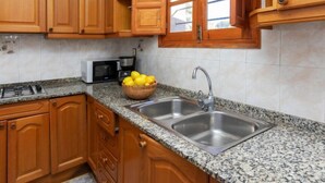 A kitchen with wooden cabinets, a granite countertop, a stainless steel sink, a microwave, and a bowl of lemons.
