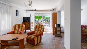 A spacious living room with a round wooden coffee table, striped armchairs, a television, and a balcony with a view of greenery. - Margaret by Interhome (Balatonfenyves)
