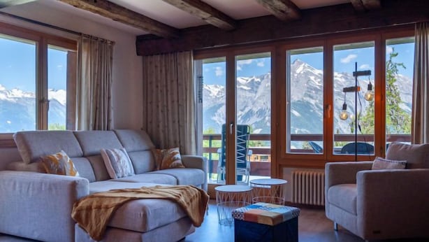 A modern living room with a sofa, armchairs, and a coffee table, large windows with mountain views, and exposed wooden beams on the ceiling. - Quille du Diable 44 by Interhome (Nendaz)