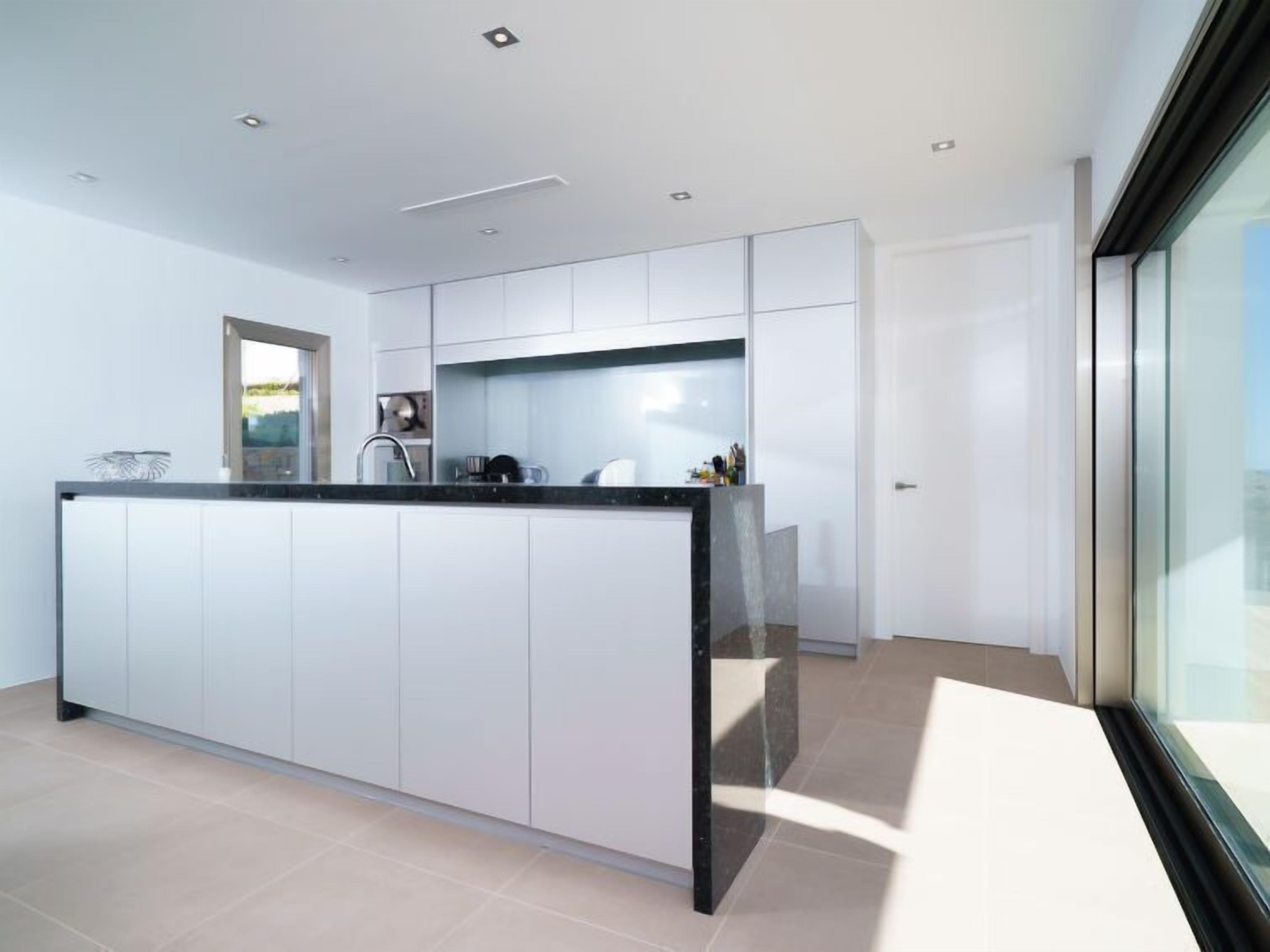 A modern kitchen with white cabinetry, a black countertop, and a large window.