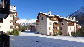 A snow-covered courtyard with buildings featuring balconies and a mountain backdrop.