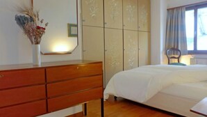 A bedroom with a wooden dresser, a bed with a white duvet, and a large wardrobe with floral designs.