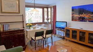 A cozy living room with a dining area, a television, and a large window with a cityscape view.