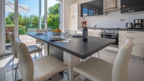 A modern kitchen with a central island, white cabinetry, and a large window overlooking a garden. - Graziani by Interhome (Krk/Kornic)