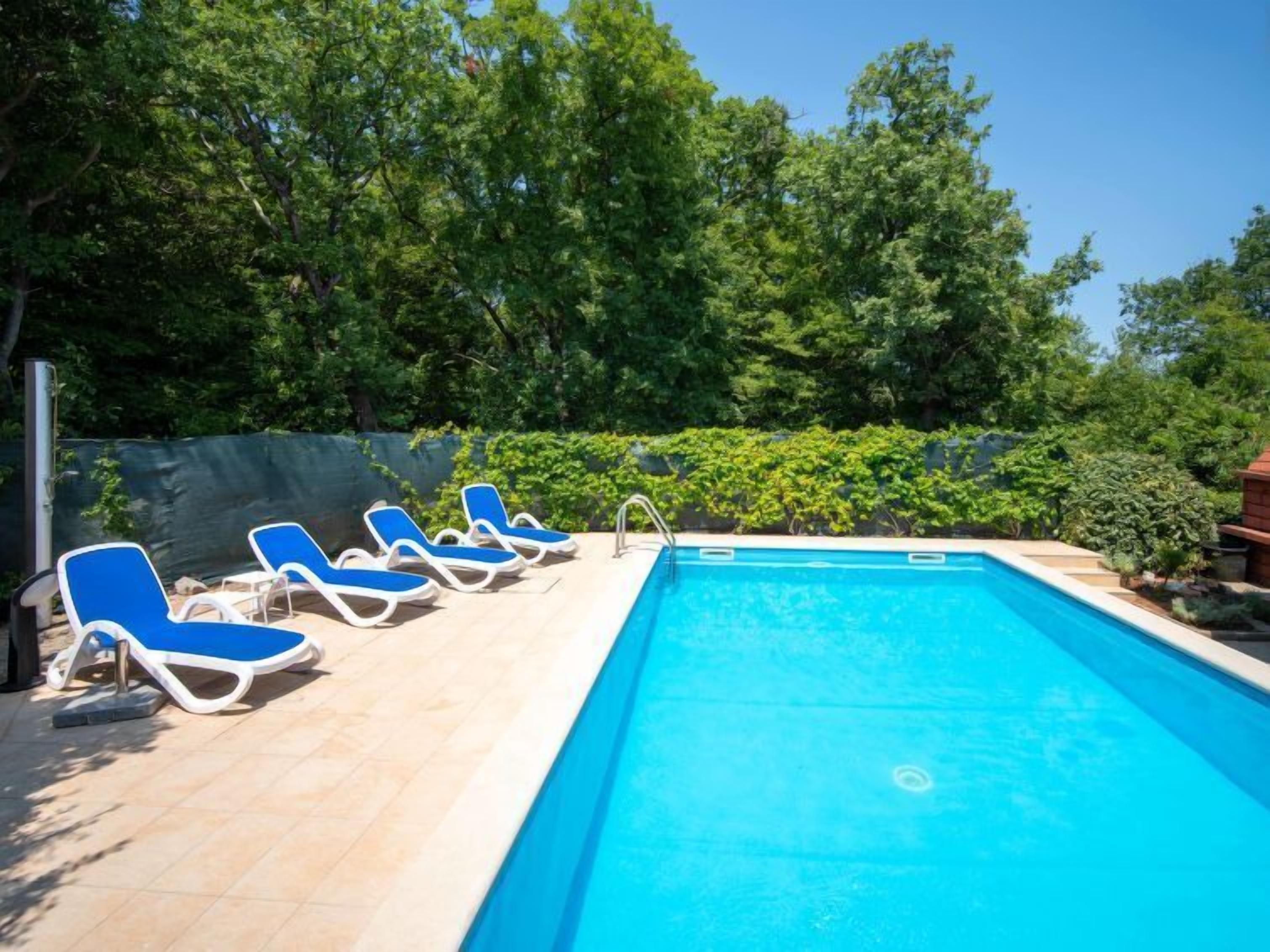 A swimming pool with blue water, surrounded by a tiled deck. There are blue lounge chairs aligned along the pool's edge.