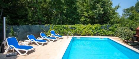 A swimming pool with blue water, surrounded by a tiled deck. There are blue lounge chairs aligned along the pool's edge.