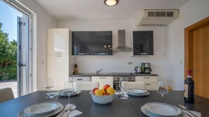 A modern kitchen with a central island, white cabinetry, and a large window. - Graziani by Interhome (Krk/Kornic)