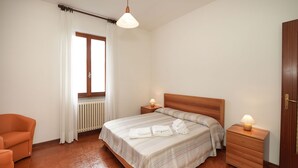 A bedroom with a bed, two bedside tables, a chair, a radiator, and a window with curtains. - Rossella by Interhome (Castelveccana)