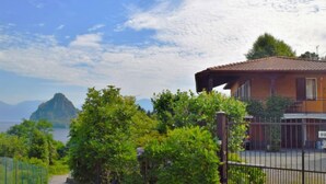 A two-story house with a balcony, surrounded by lush greenery and a view of a mountain and sea. - Rossella by Interhome (Castelveccana)