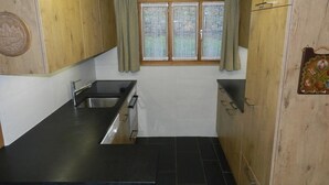 Een compacte keuken met een zwart aanrecht, een roestvrijstalen spoelbak en houten kastjes.