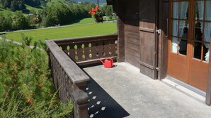 Een houten gebouw met een balkon met uitzicht op een groen landschap en bergen.