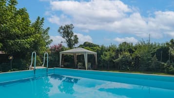 Una piscina cristallina con area relax coperta e rigogliosa vegetazione sullo sfondo.