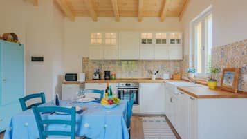 Una cucina con mobili bianchi, soffitto in legno e zona pranzo con tovaglia e sedie blu.